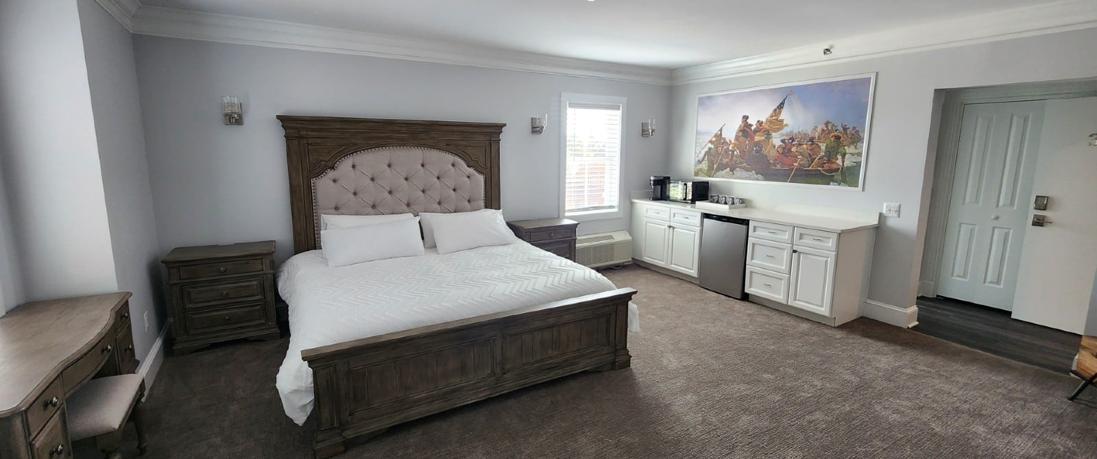 Spacious bedroom with king bed, kitchenette counter, two side tables and writing desk with stool