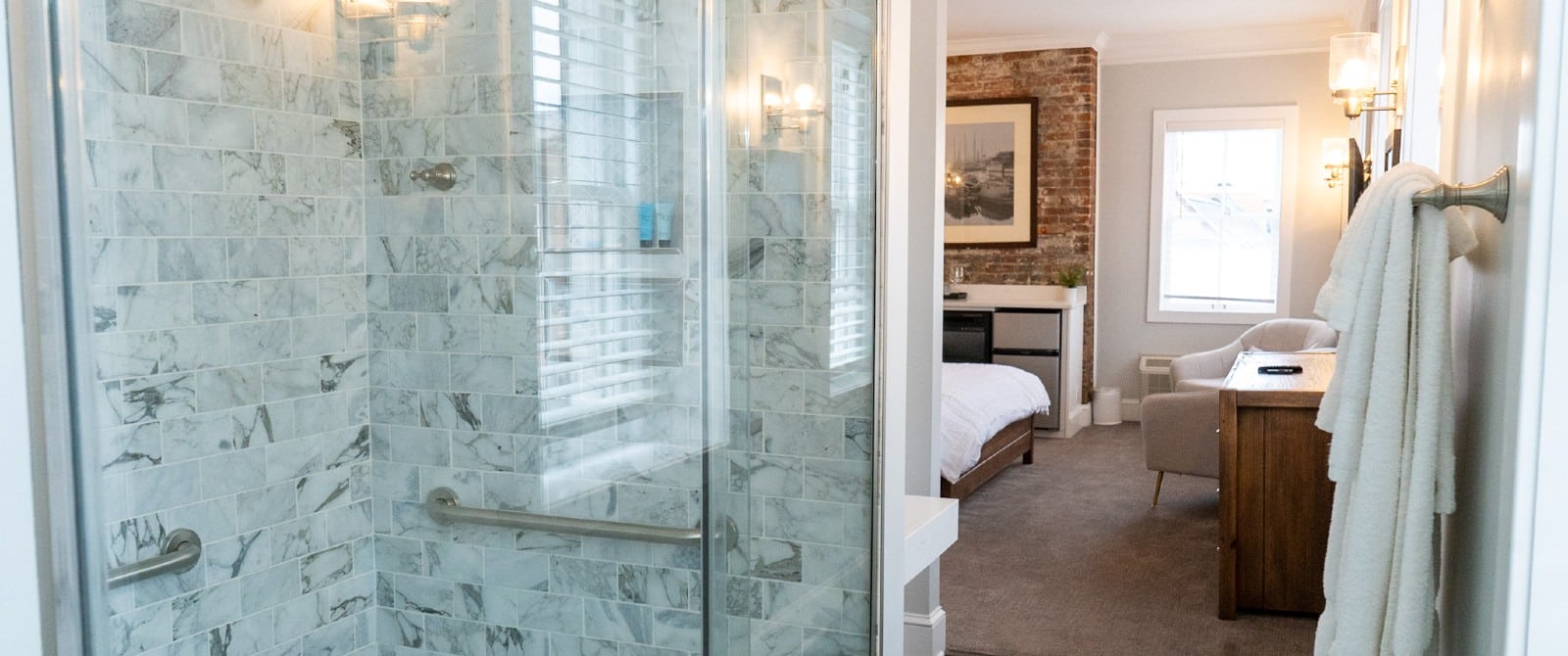 Open bathroom with tiled shower and glass doors overlooking spacious bedroom