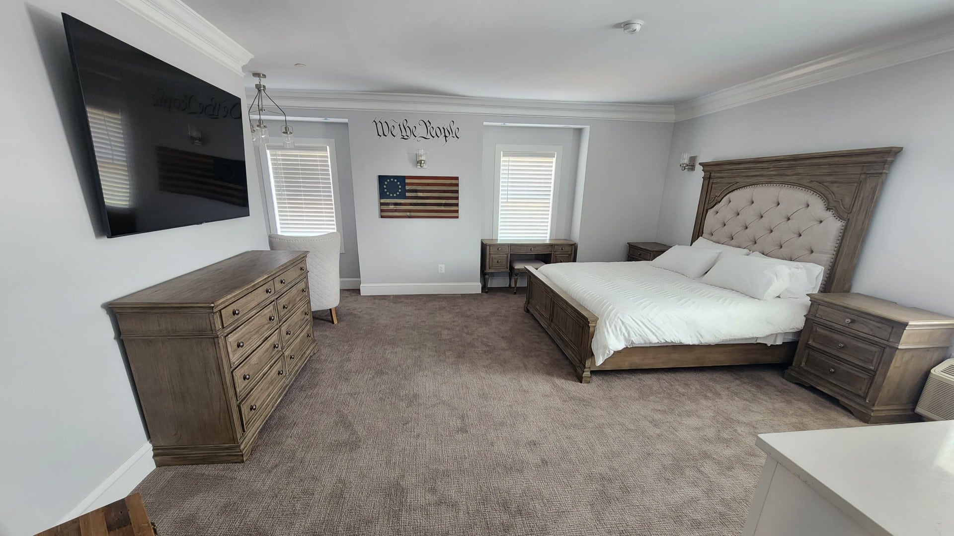 Large bedroom with king bed, TV over a dresser, two side tables and windows with blinds